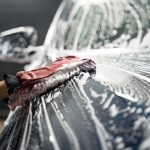 Professional car wash. Detailing worker washes the vehicle body with foam and rag